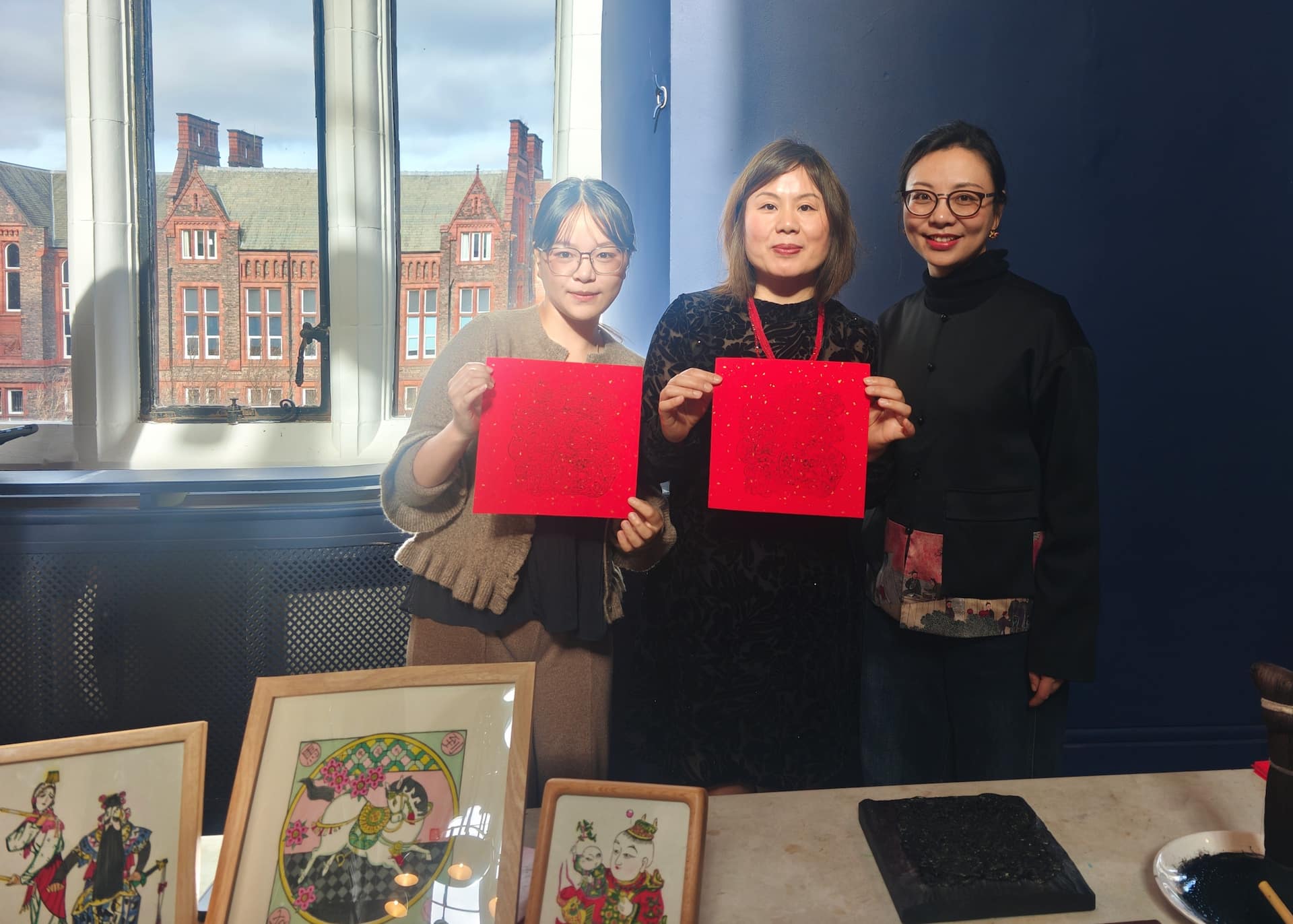 Three people standing in front of Chinese embroidery and holding up wood block prints.