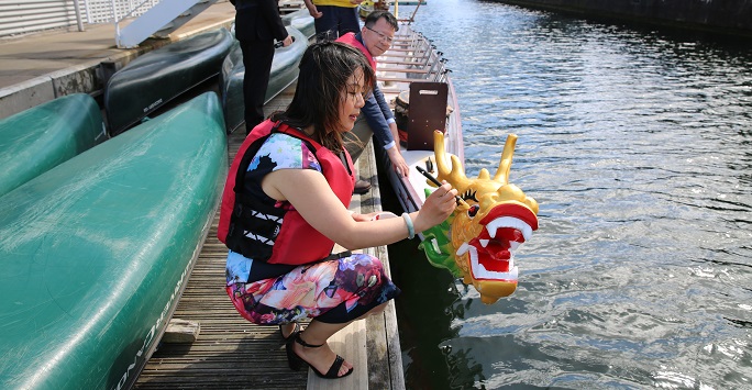 woman dotting eyes of a dragon boat with red paint
