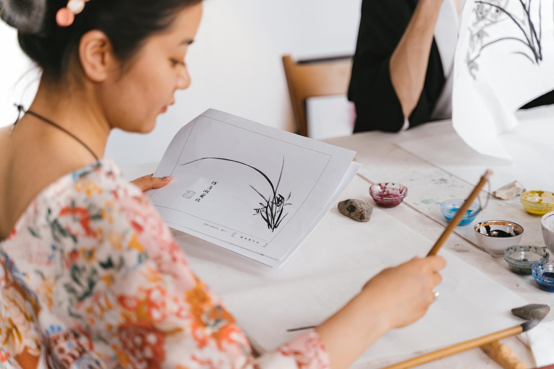 A person drawing with Chinese ink, following instructions from a printed diagram
