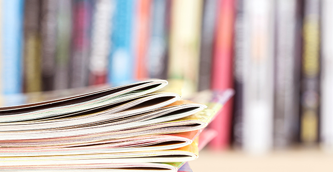 Close up edge of colorful magazine stacking with blurry bookshelf background