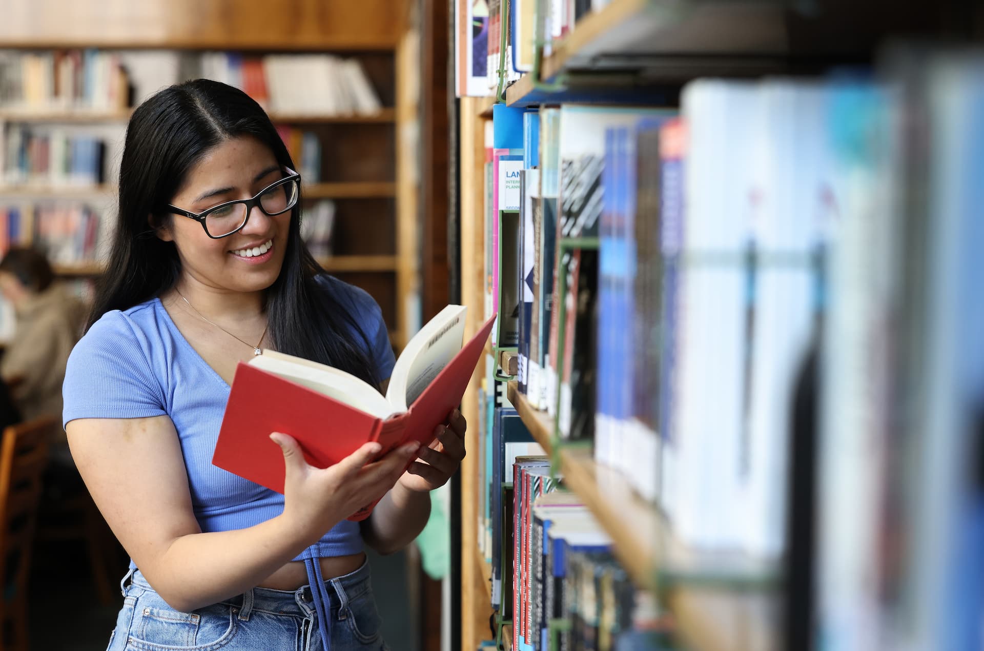 A student reading a book next to a book shelf.