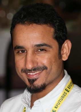 A smiling man with a dark beard wearing a light yellow shirt and bright yellow lanyard which says EFUTURES