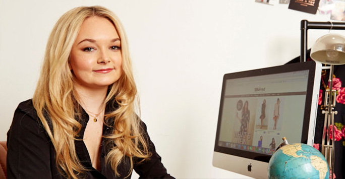Emma Watkinson sitting in front of computer monitor showing SilkFred website
