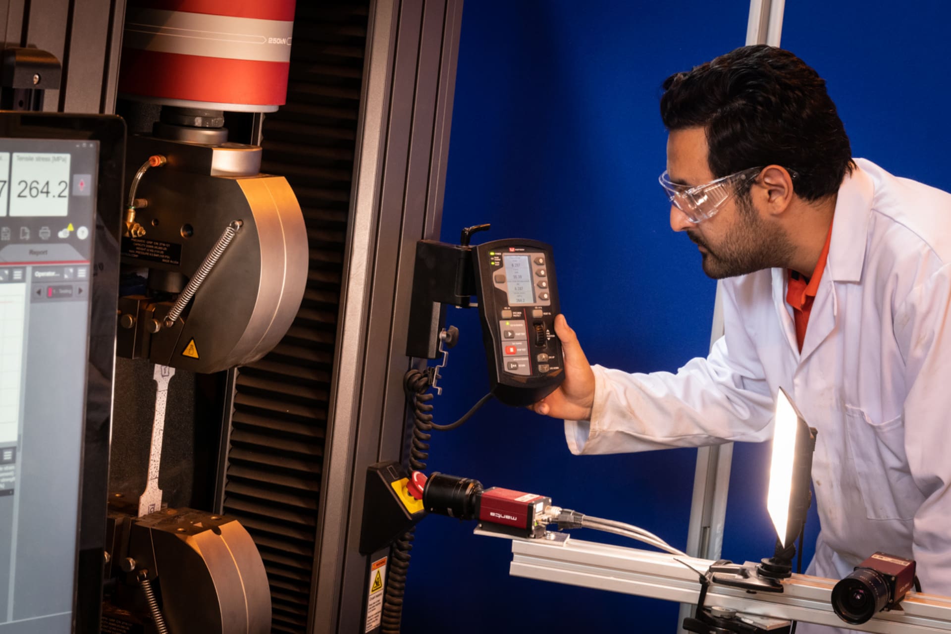An engineering student wearing a white lab coat adjusting a machine.