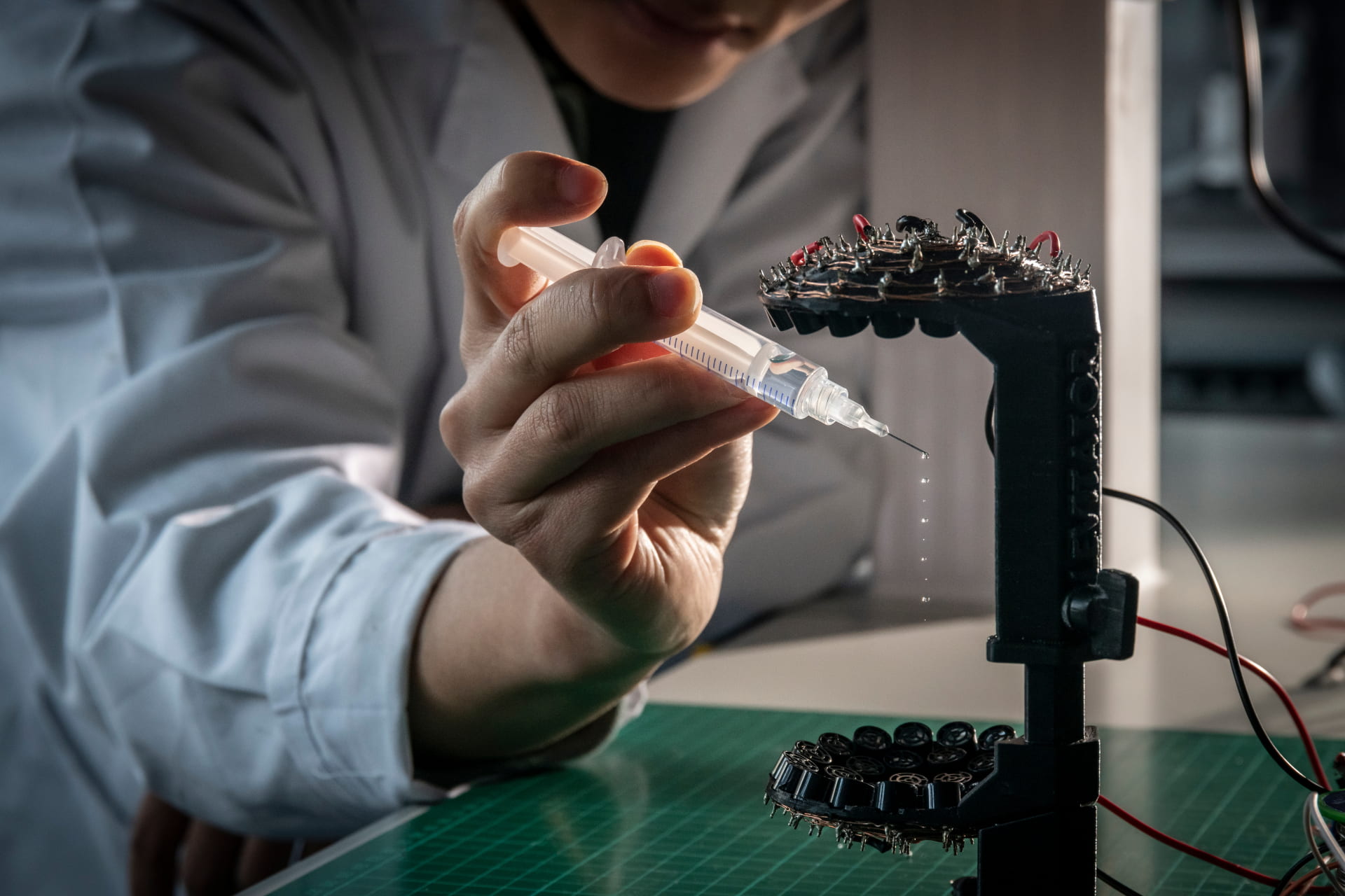 A hand holding a syringe drips water onto a complex electrical device.