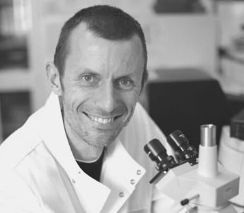 Greyscale portrait on white male with short brown hair sat by microscope