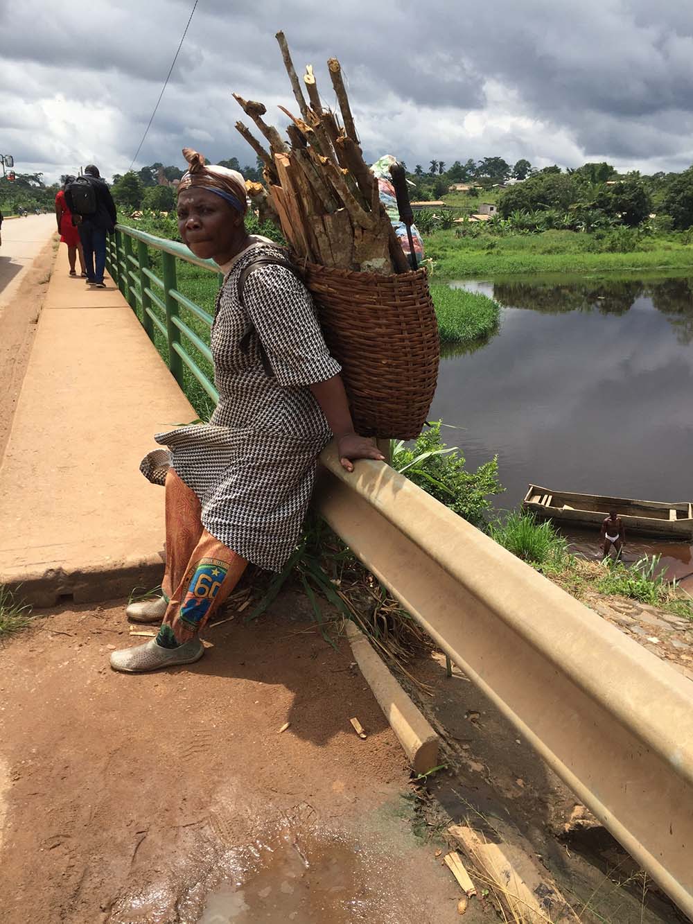Cameroonian woman crossing bridge carrying bag of fire wood