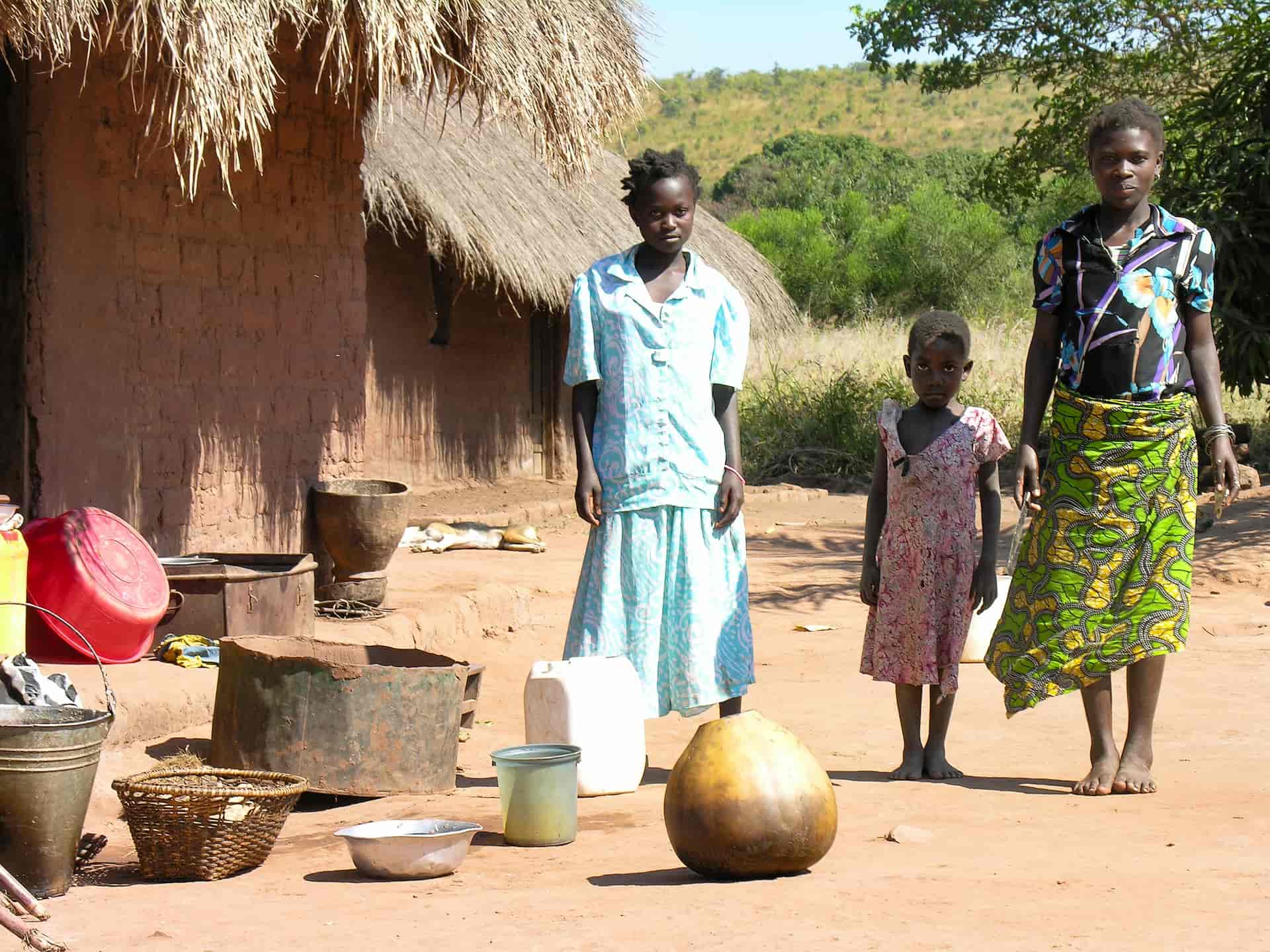 Group of Congolese women and young girl stand next to their home