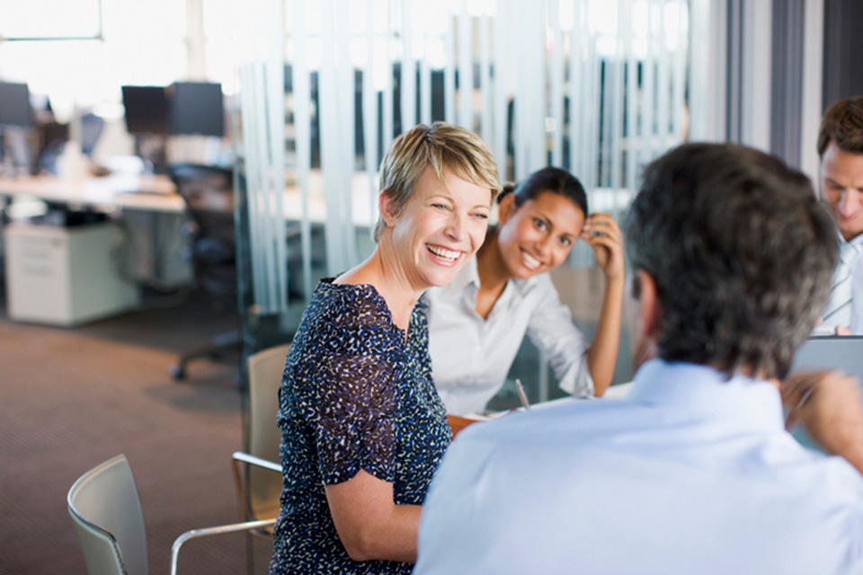 Colleagues sitting around a table smiling as they work collaboratively.