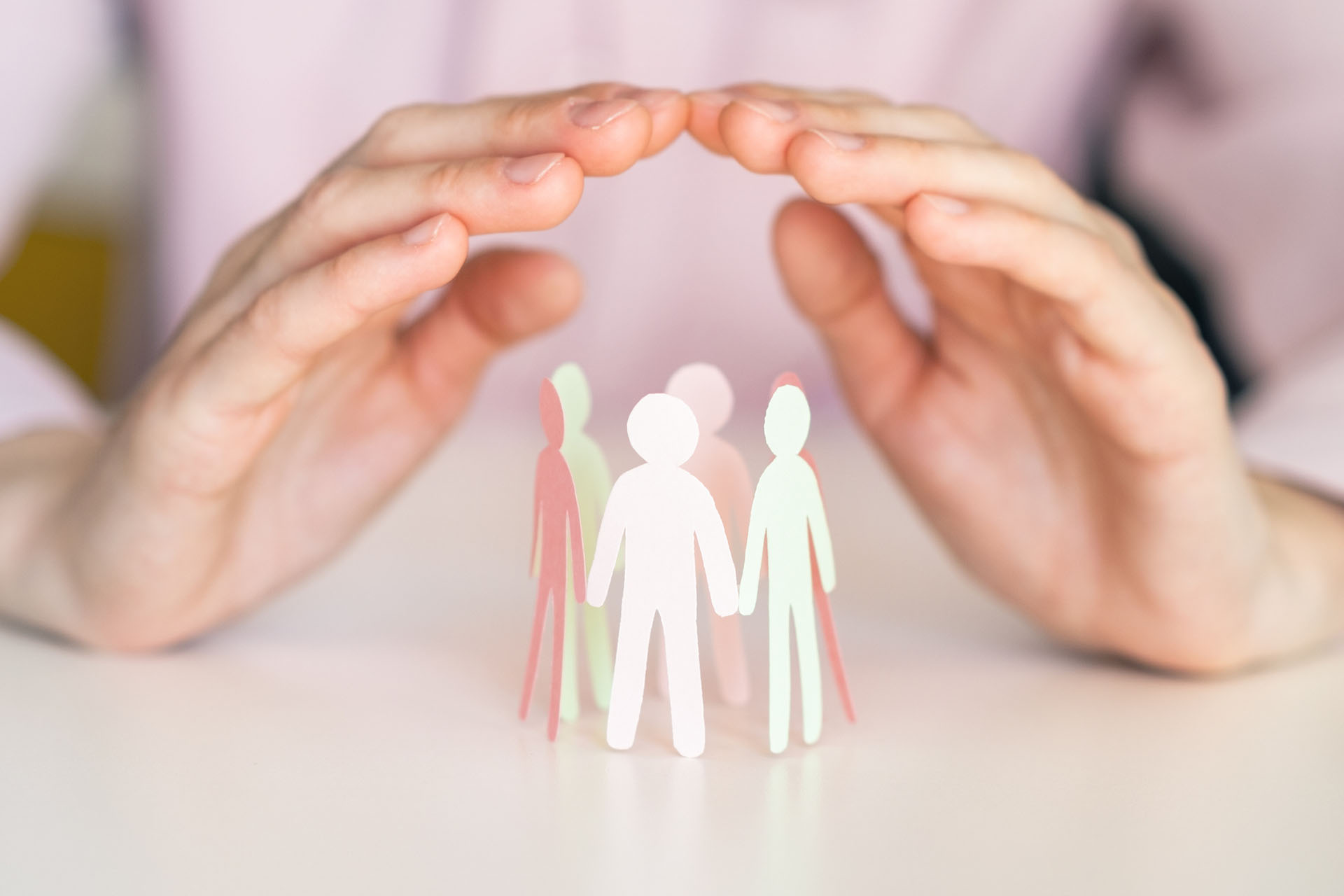 image of two hands clasped over a paper cut out of a family holding hands in a circle.