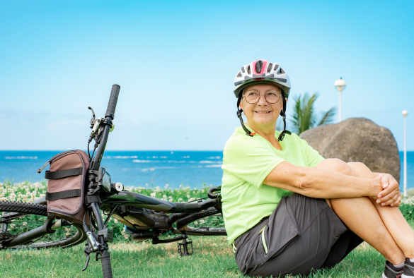 image of elderly woman sitting on gras field with her bike and a helmet on.