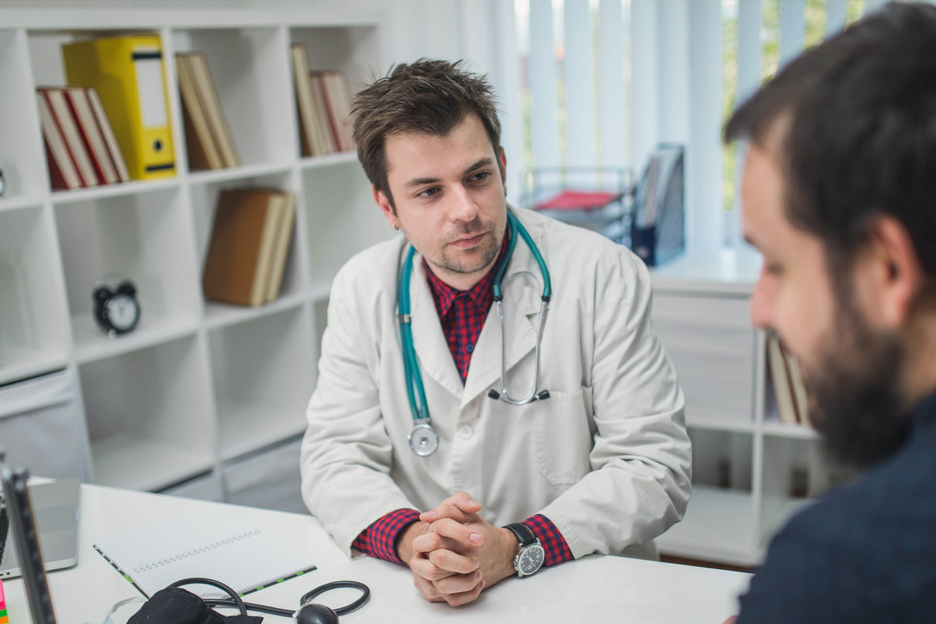 Young doctor sitting at a desk talking to a male patient