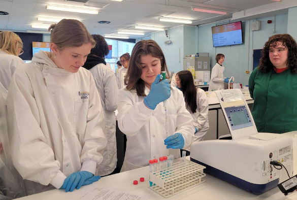 Students in the Life Sciences laboratory, dressed in white lab coats, blue gloves, using a pipette