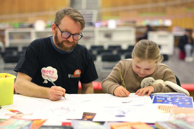 A male volunteer and a child colouring and drawing
