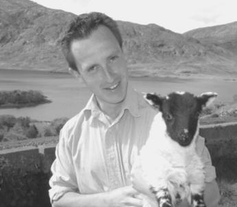 White male with dark hair holding a lamb and looking at the camera