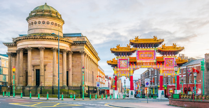 The ornate, vibrant, and colourful Chinese arch in Liverpool, next to a historical building with a round dome on top and columns out front.