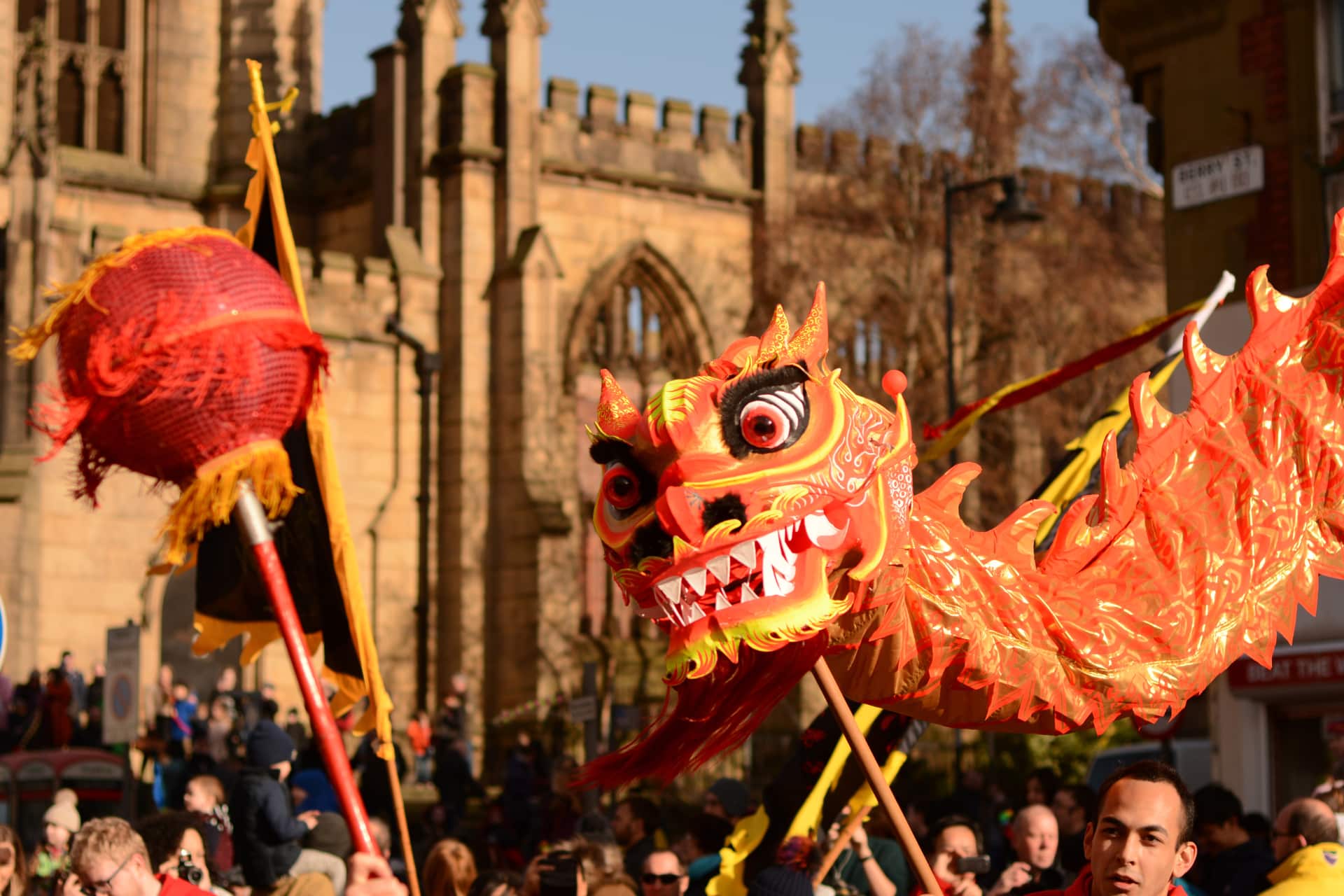 A bright red dragon puppet is dancing above a crowd in front of Liverpool's Bombed-out church, chasing a red circle on a stick.