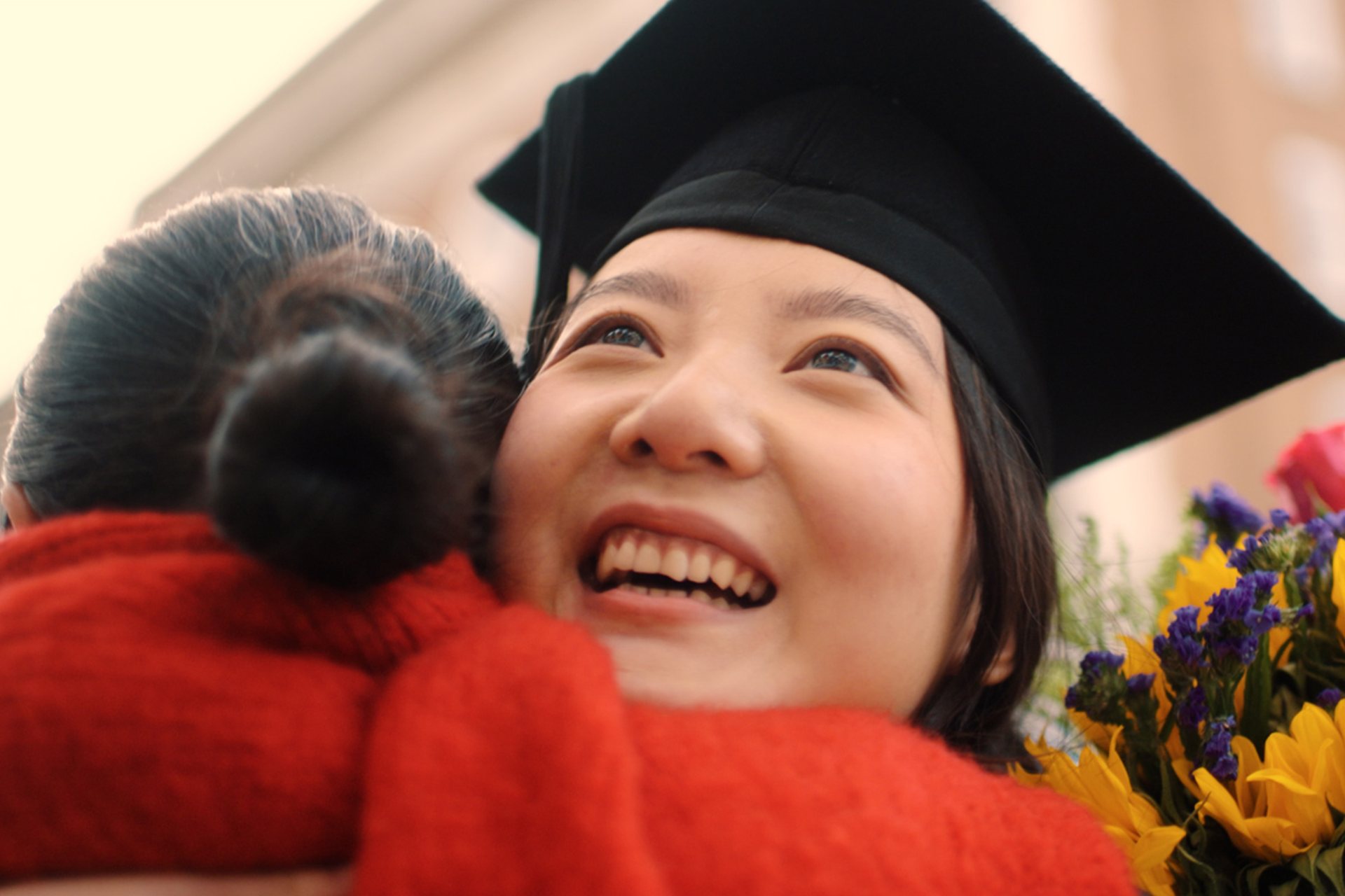 A student dressed in their graduation cap and gown hugging a family member.