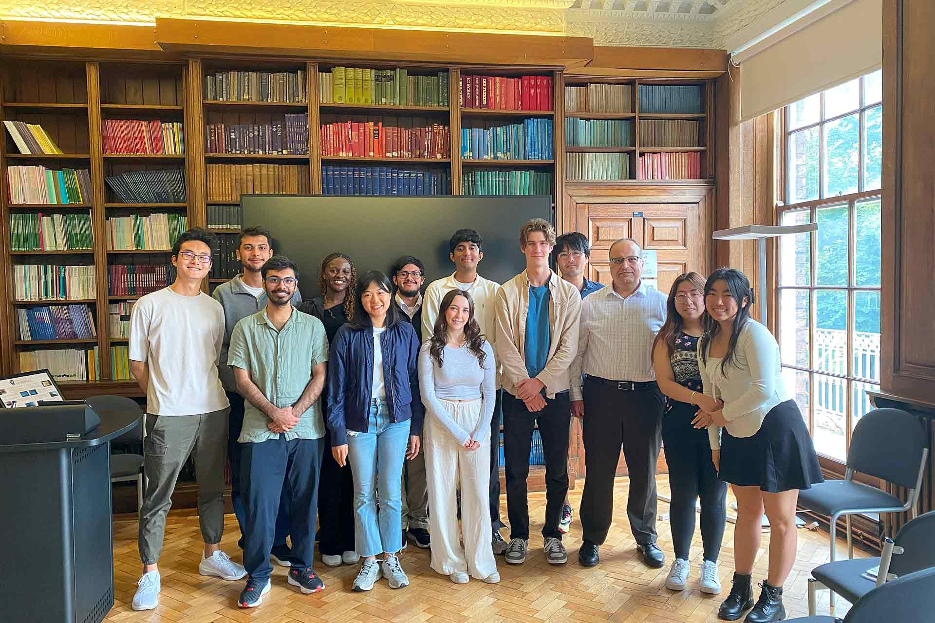 A group of inbound Global Opportunities students stand in front of bookshelves in the Harold Cohen Library