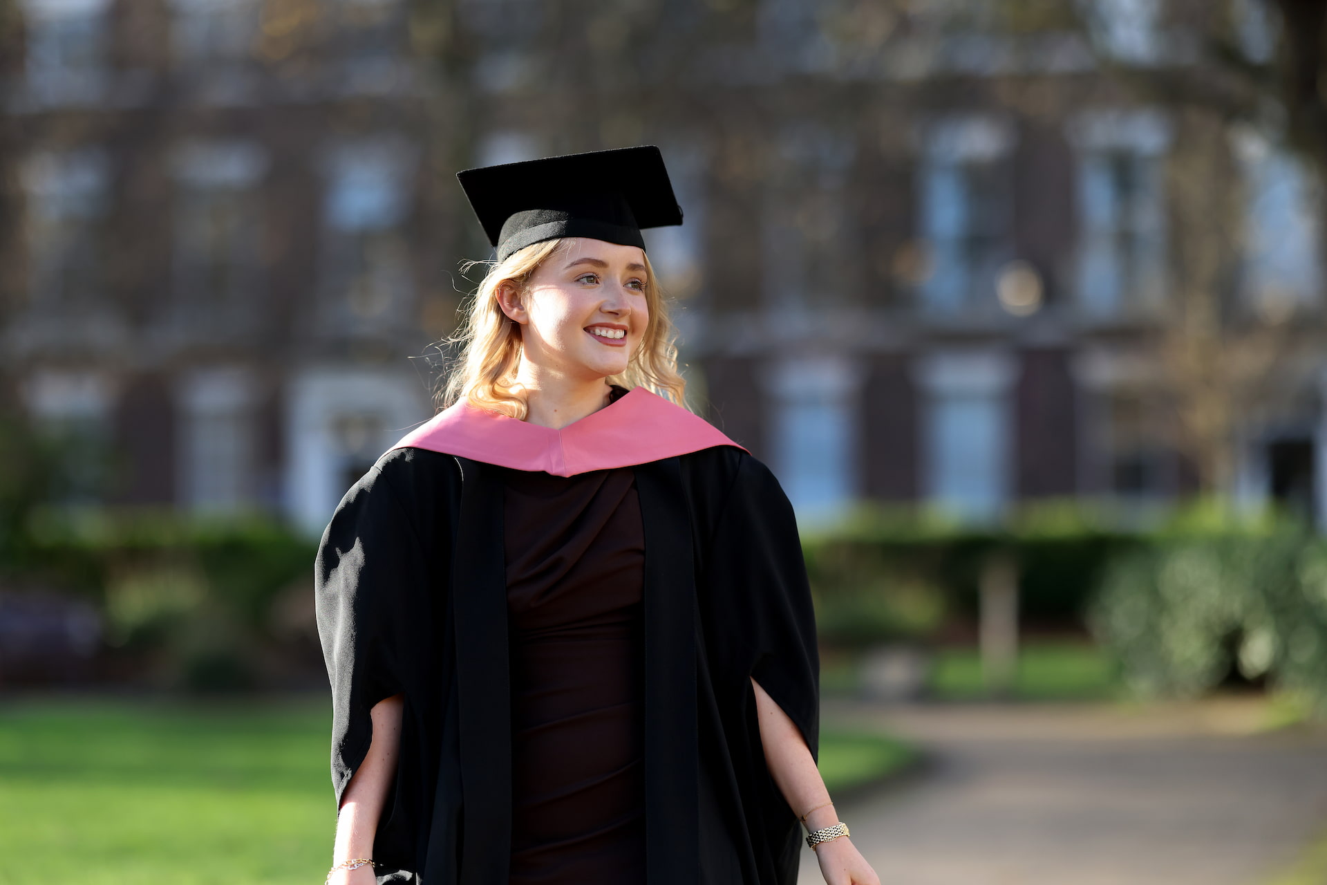 A student in a gown standing in the sun on graduation day