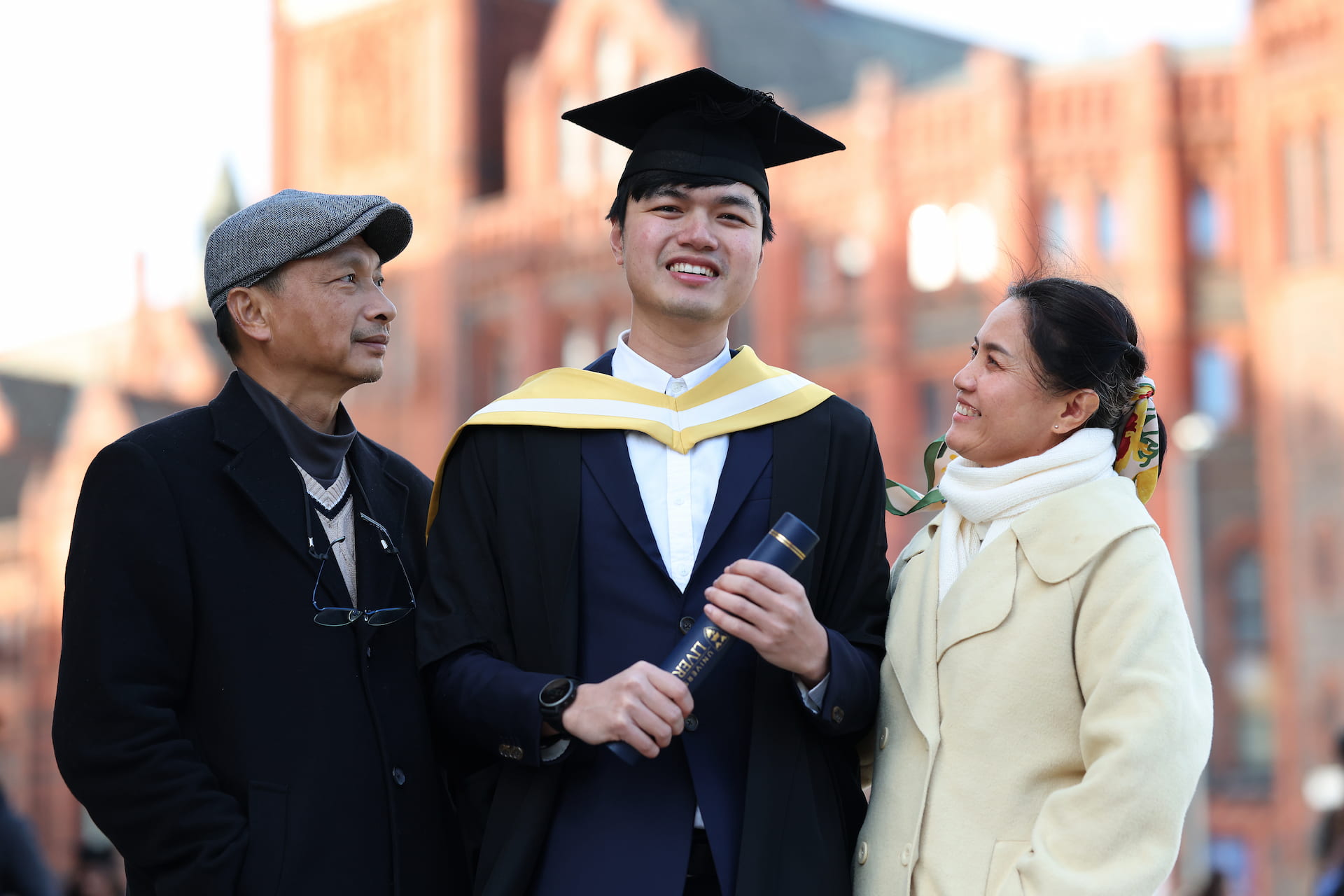 A student holding his degree with proud parents on graduation day