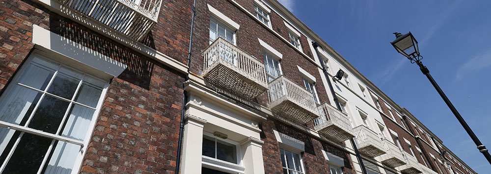 Looking up at a three-story historic terrace with brown brick and white paintwork