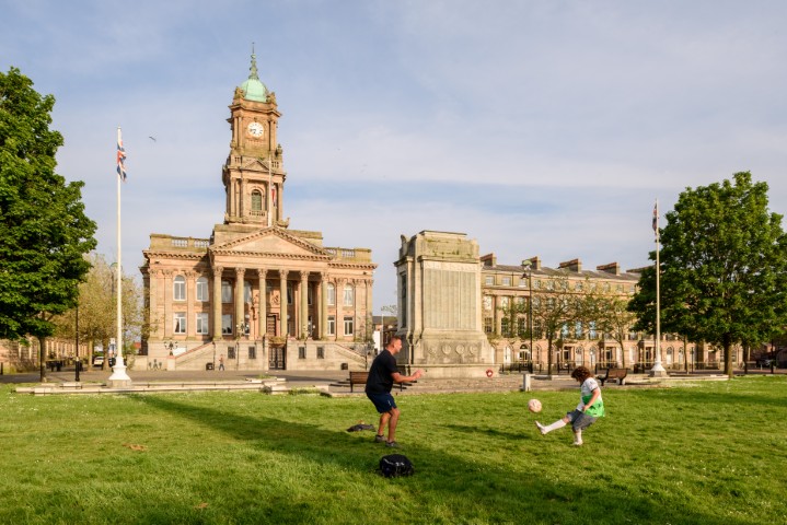 Man and boy playing football on grass in front of Birkenhead Town Hall