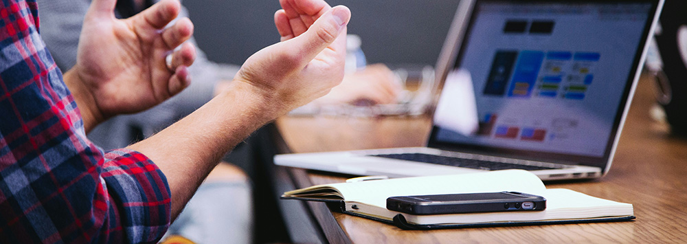 The hands of a person sitting at a meeting table with a laptop, notebook and phone