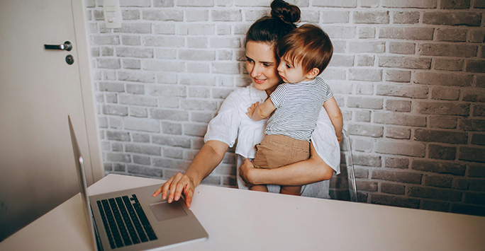 A woman holding a child while working at a laptop