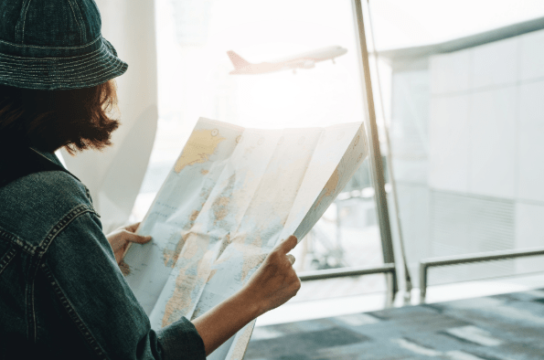 A girl holding a map, a plane flies off in the distance