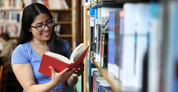 Student in library reading a book and smiling
