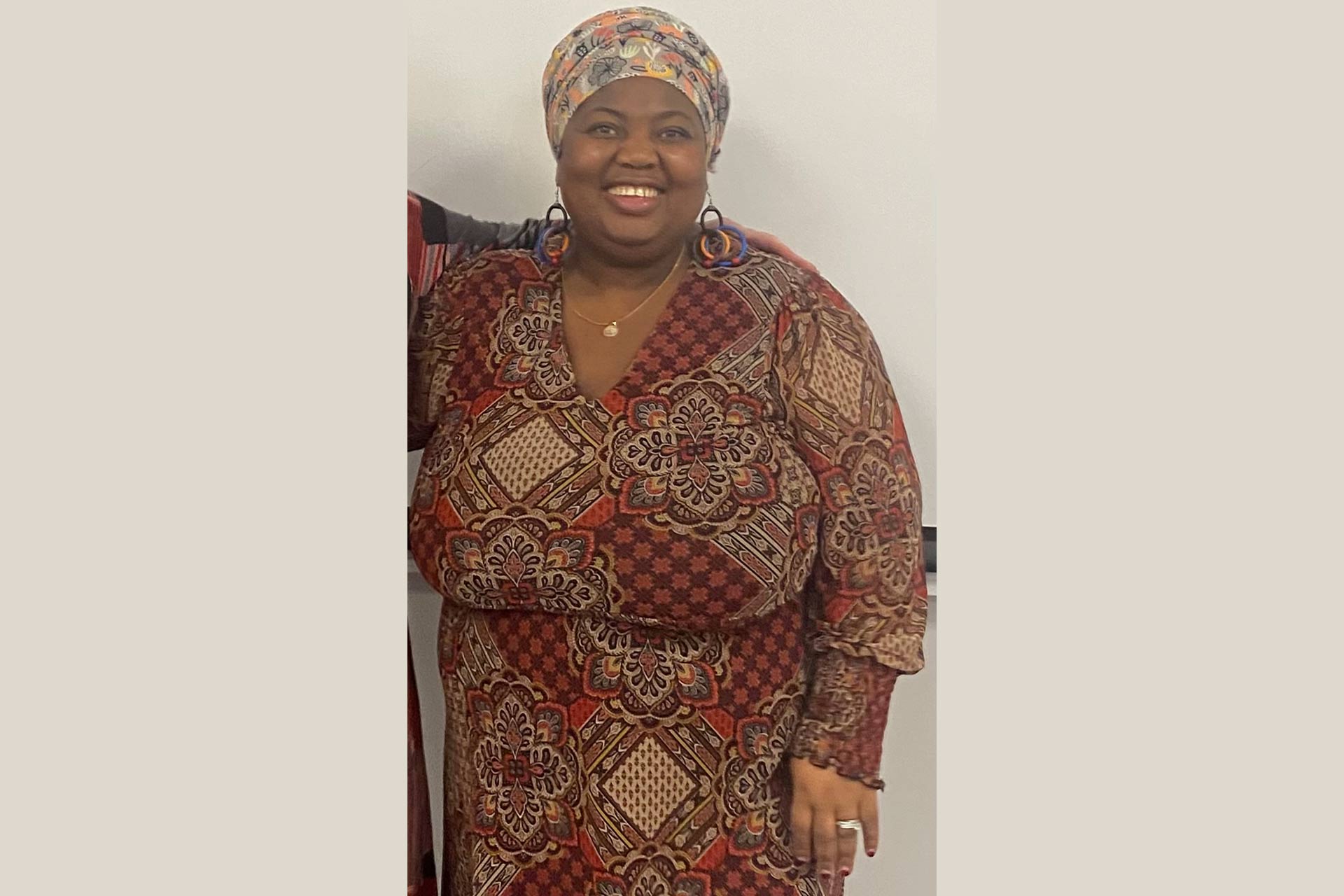 Tracy Mpofu is a Black woman wearing a colourful patterned dress and headcovering.