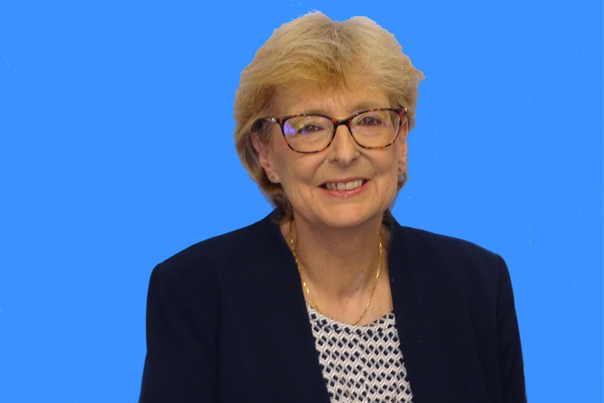 An older woman with blonde short hair and glasses and a smart blazer smiling.