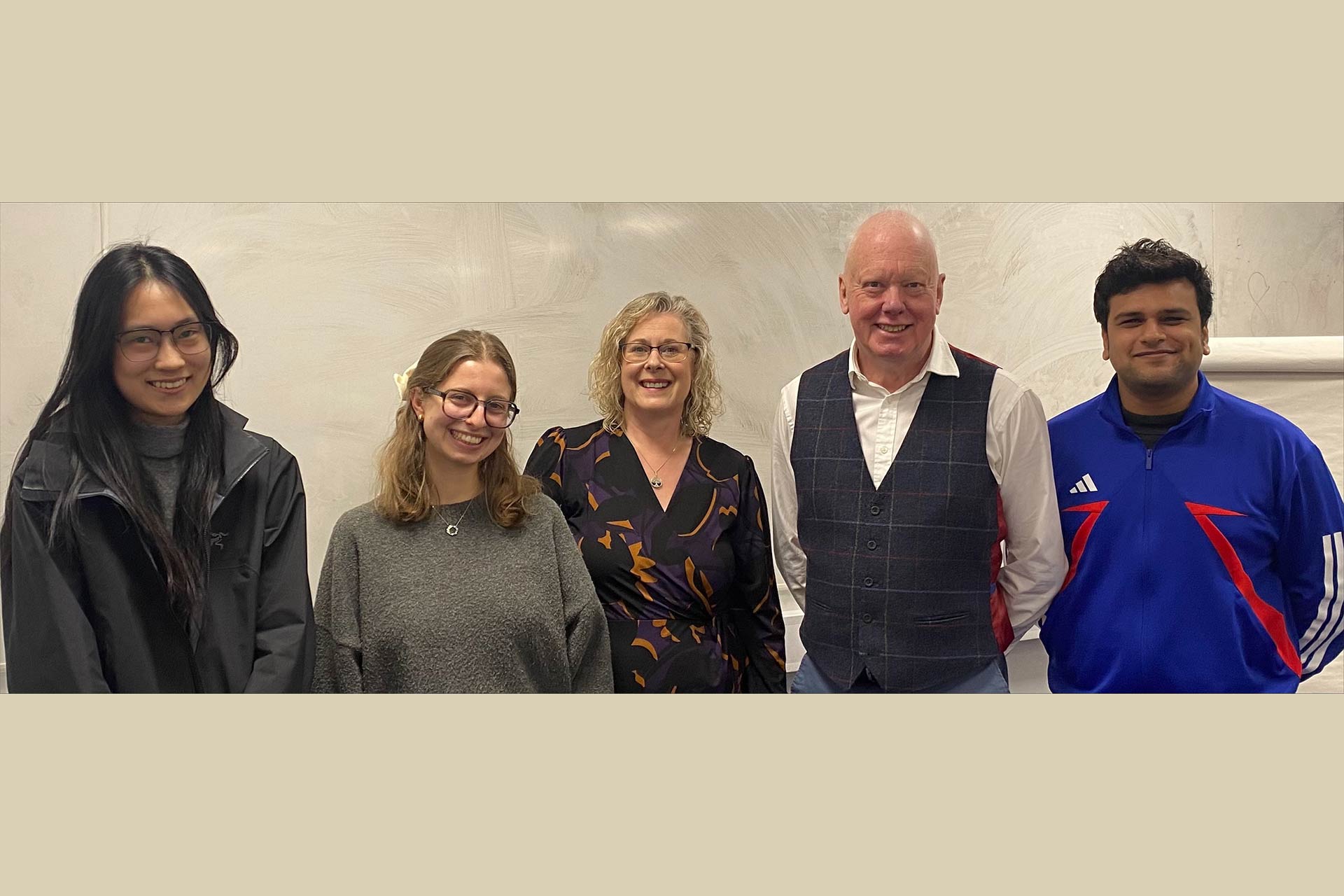 5 people standing together in a line smiling in a classroom.