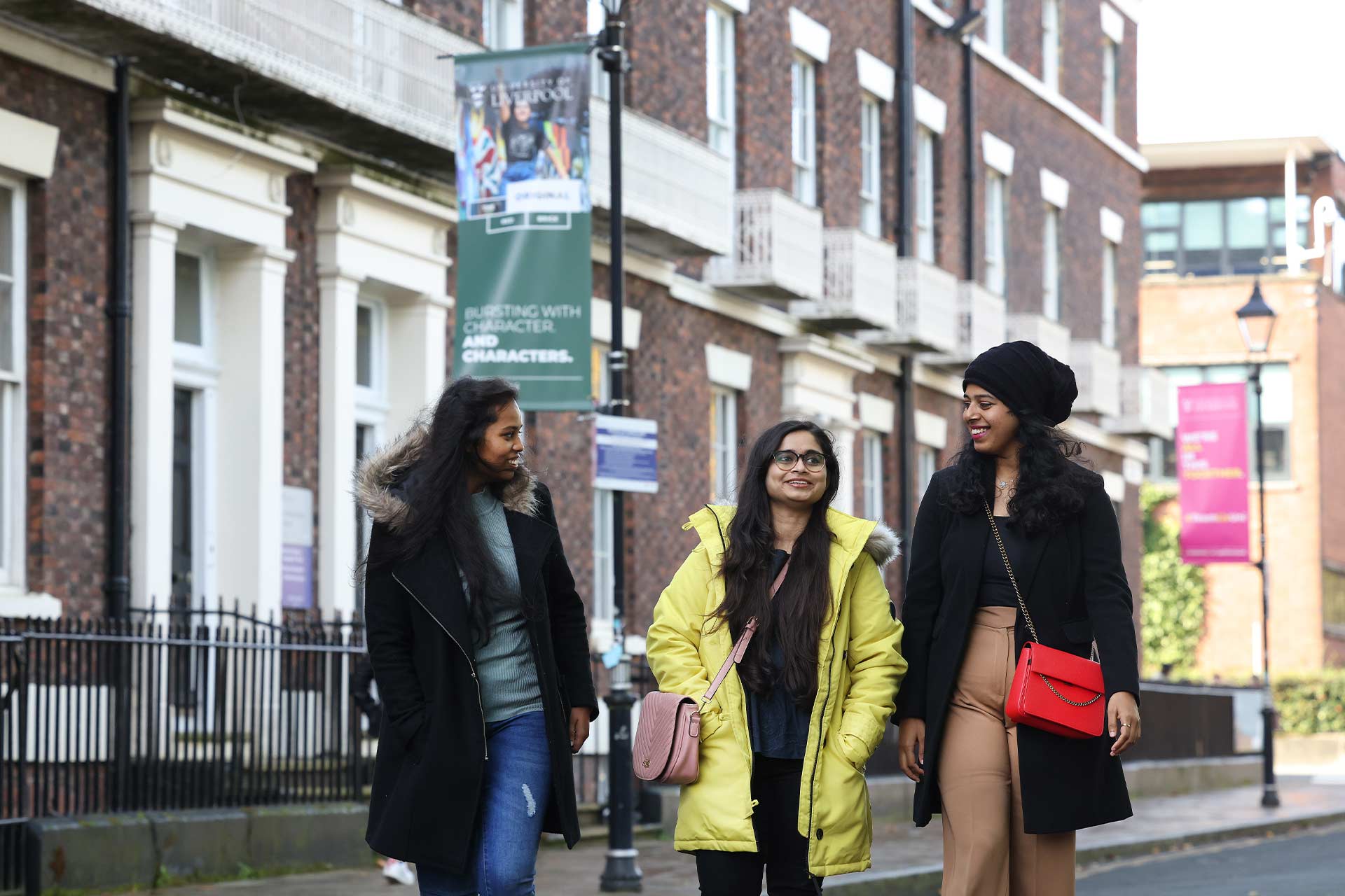 Three students walking outside talking and laughing by Georgian terraced houses on a university campus.