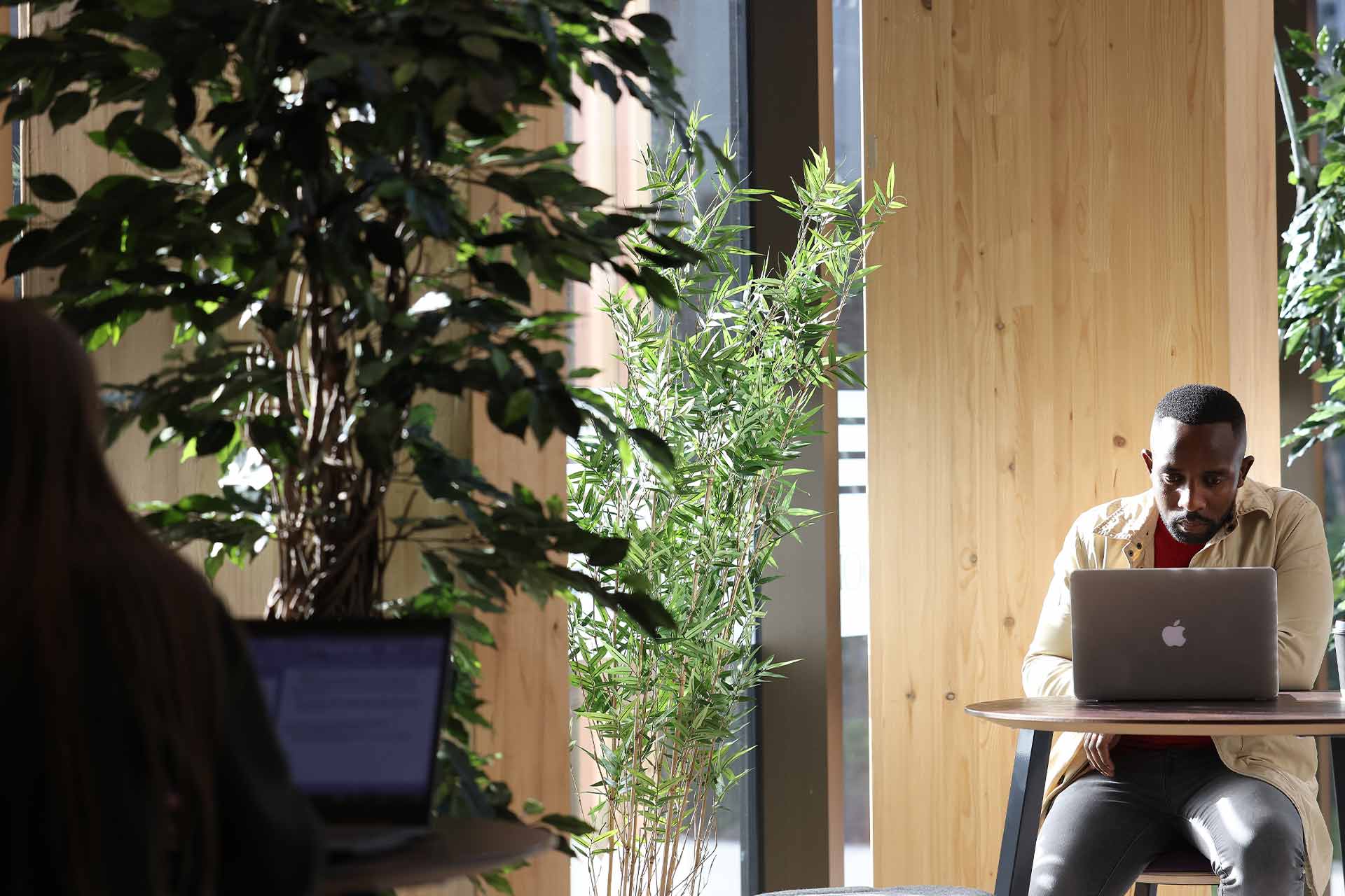 A man sitting at a desk inside, working on a laptop.