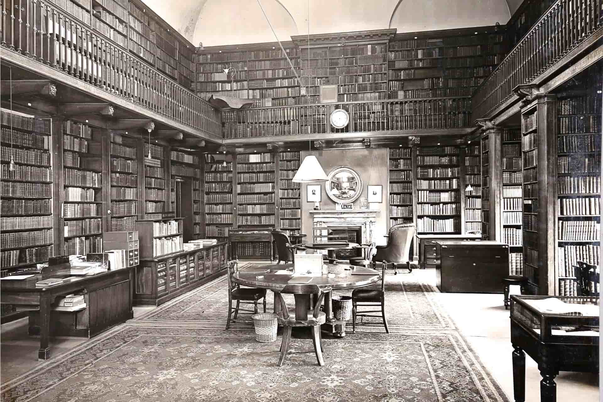 A sepia image of an old library with dark wooden bookcases and furniture.