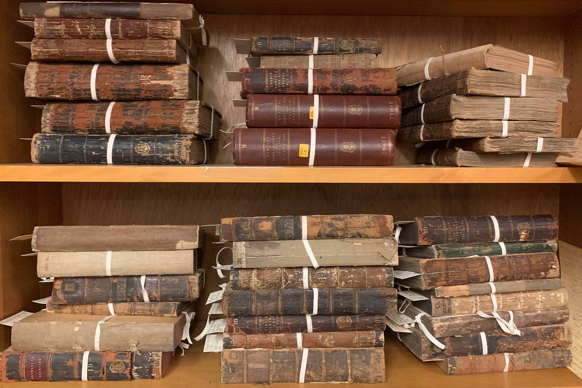 Two shelves of old slightly worn books in piles.