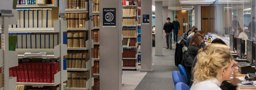 Students in library on computers near bookshelves.