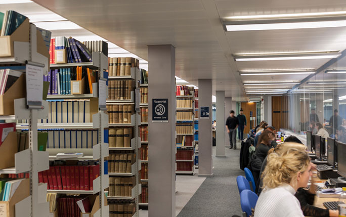 Students in library on computers near bookshelves.