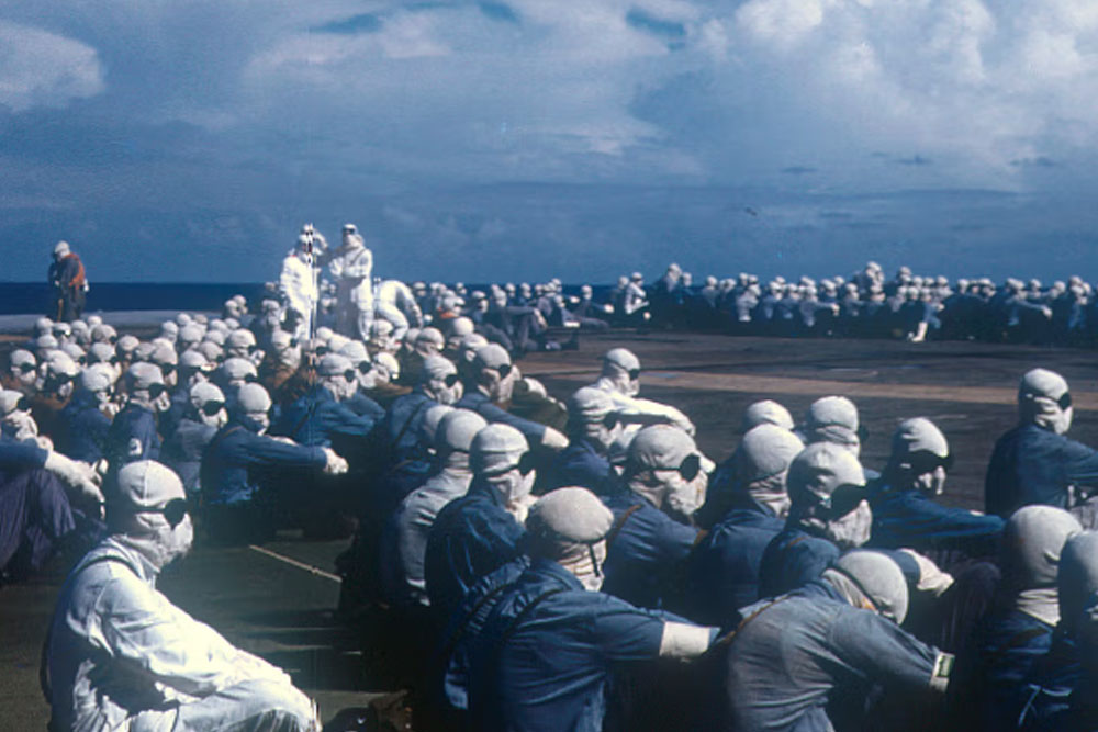 Service personnel wearing goggles and hoods sitting down waiting to observe a nuclear detonation.