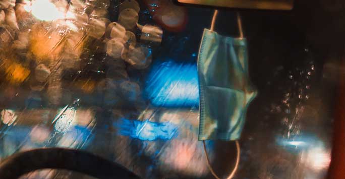 A face mask hanging from a car's rear view mirror