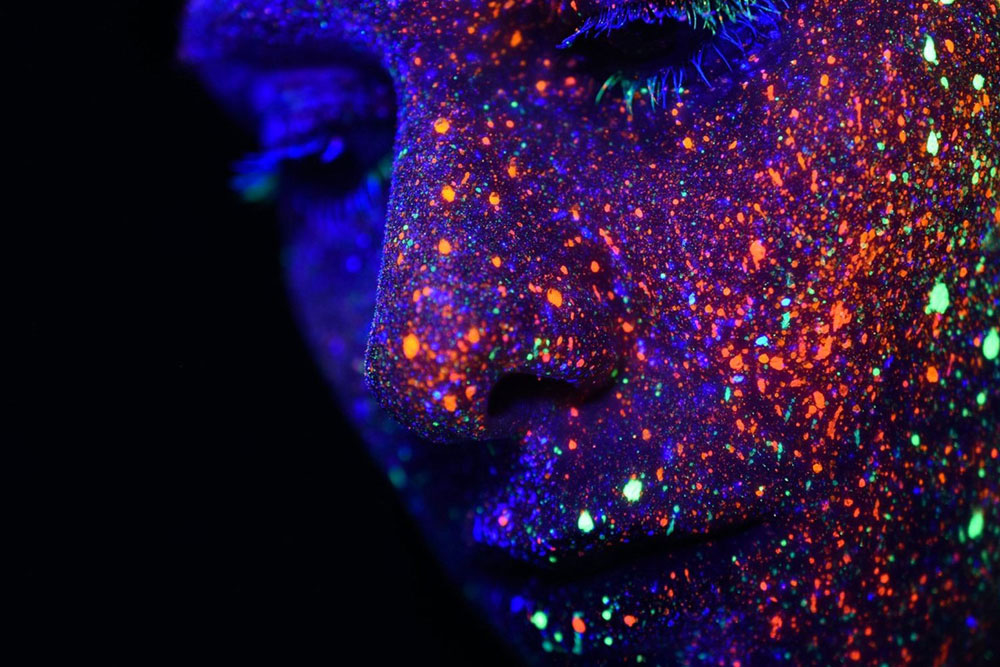 A face against a dark background with day-glo paint splashes