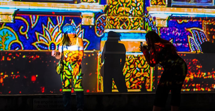 A woman having her photograph taken against a digital projection