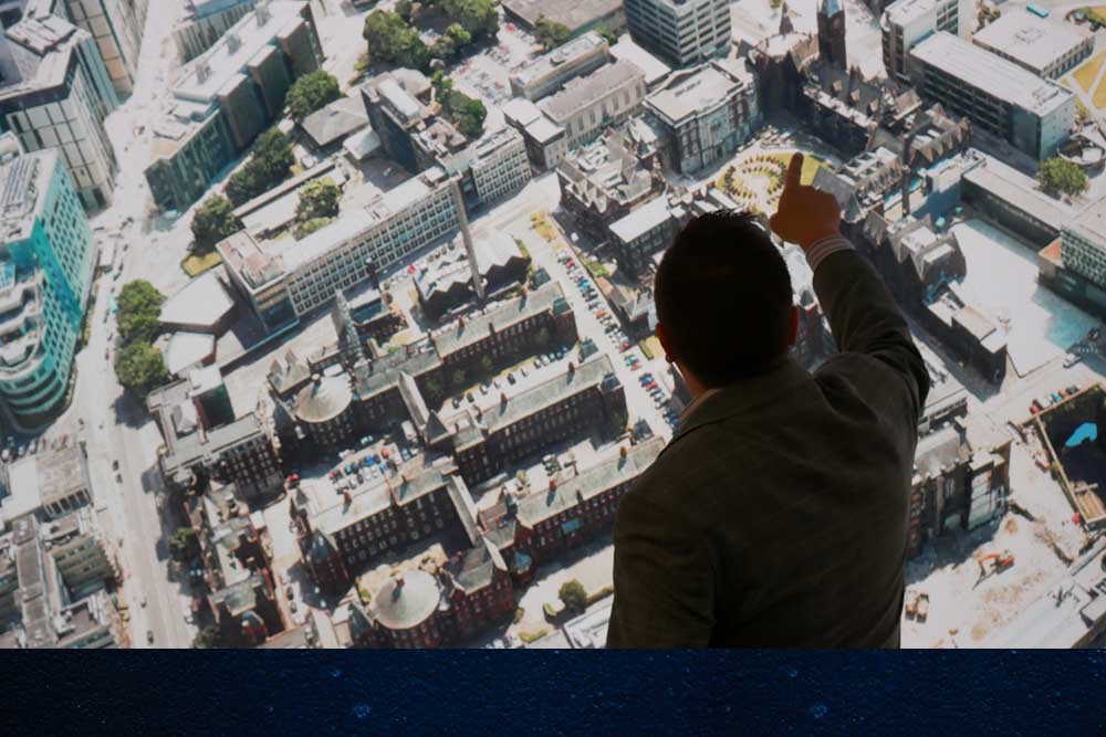 A man, seen from behind, pointing at a large aerial view of Liverpool