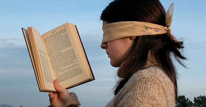 A blindfolded woman looking at a book