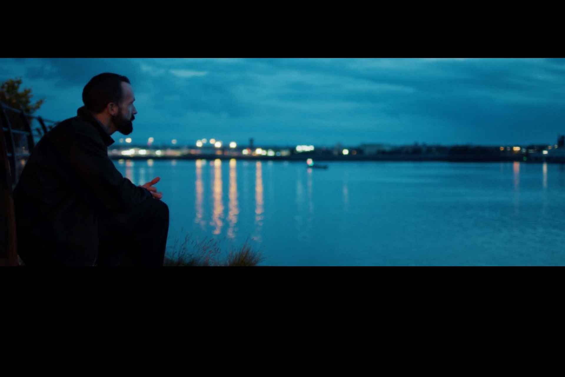 A man looking across a river at night