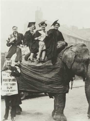 A black and white photo of students, some in cap and gown, sitting on an Indian elephant