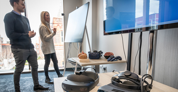 2 people standing talking at a whiteboard