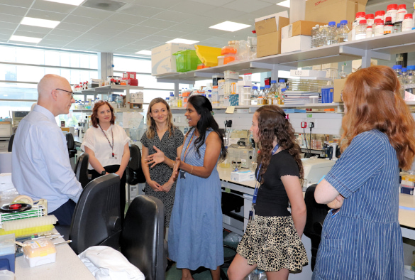 Microbiology researchers in the lab discussing their research with a man and a woman from the Microbiology Society